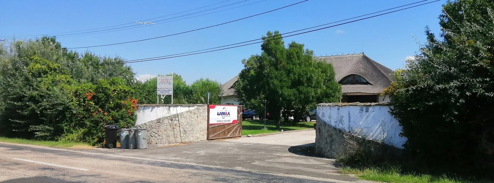 Az Agárdi Autójavító bejárata: terméskő kerítés, fa kapu és a nádtetős műhelyépület Pákozdon